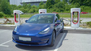 Güneşli bir yaz gününde, işlek otoyolda yeni model 3 Tesla ücret alıyor.