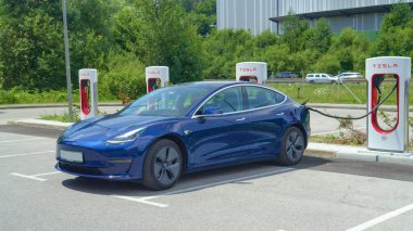 Özerk Tesla arabası yoğun bir otoyol tarafından şarj edilen bir terminale bağlanır.