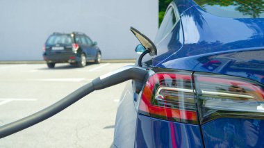 Parlak, yeni bir Tesla arabasının bir otoparkta şarj olurken detaylı görüntüsü..