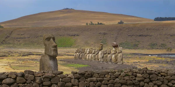 Misteriosas estructuras monolíticas con un rostro humano están detrás de una pared baja de rocas. — Foto de Stock
