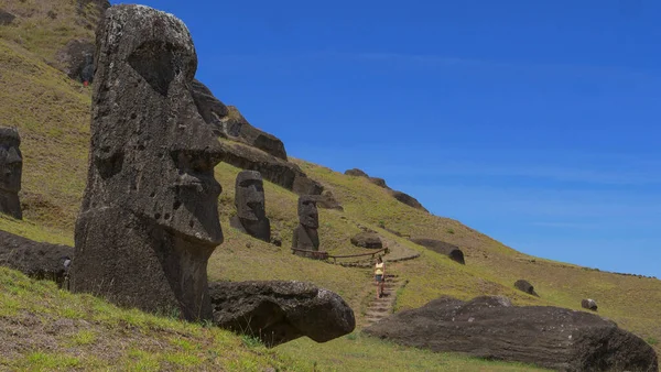 ΧΑΜΗΛΗ ΑΓΓΛΙΑ: Περίεργη γυναίκα τουρίστρια περπατά κατά μήκος ενός μονοπατιού που τρέχει παρελθόν αγάλματα Moai. — Φωτογραφία Αρχείου