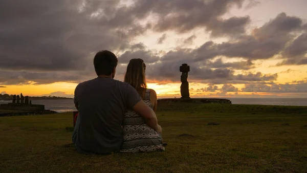 CLOSE UP: Junges Touristenpaar sitzt und kuschelt, während es Moais bei Sonnenuntergang beobachtet. — Stockfoto