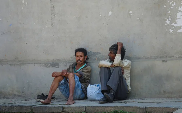 Κοντινό πλάνο: Δύο ντόπιοι άνδρες κάθονται στο τσιμεντένιο πεζοδρόμιο και παρατηρούν τη ζωή της πόλης. — Φωτογραφία Αρχείου