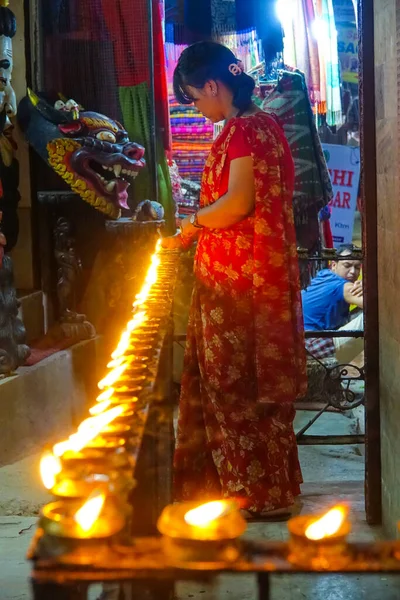ПІДКАЗКА. Місцева жінка в червоному платті запалює свічки олії в темному храмі.. — стокове фото