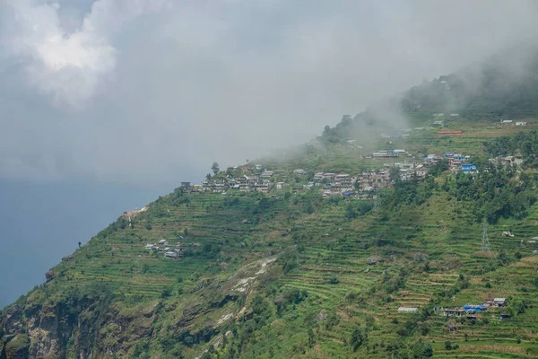 AERIAL: Witte wolken drijven over het landelijke dorp op de steile heuvel in Nepal. — Stockfoto