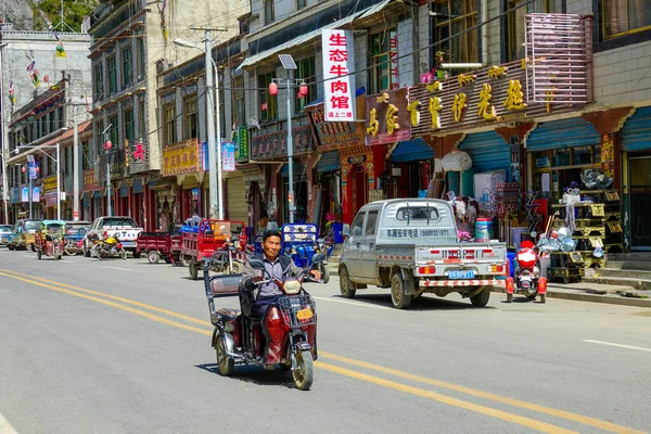 Lokal tibetansk man rider sin gamla motorcykel trehjuling genom den färgglada staden. — Stockfoto