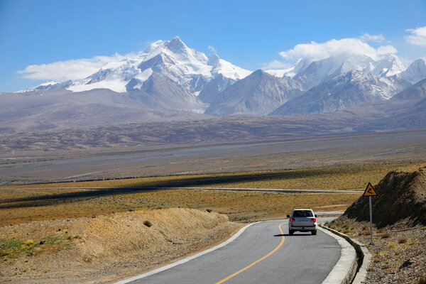 White SUV drives down an empty asphalt road leading to the snowy mountains.