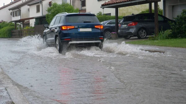 CLOSE UP: Blue SUV drives through the flooded streets of a suburban neighborhood — Stock Photo, Image