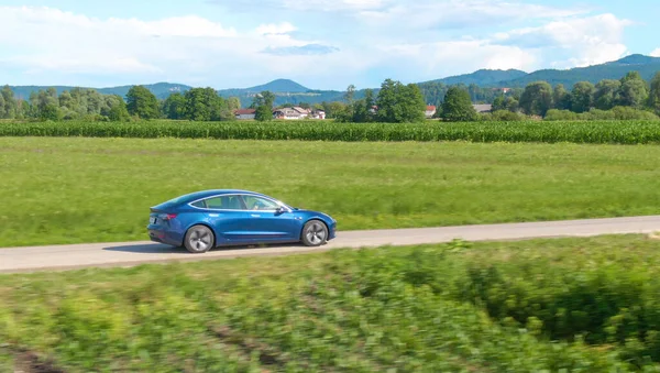 DRONE: Shiny blue Tesla drives along a scenic country road on a sunny spring day — Stock Photo, Image