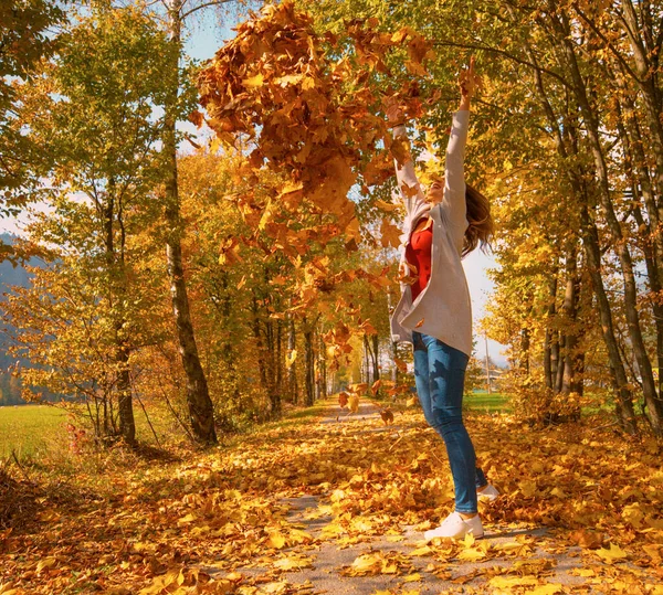 Biała kobieta stoi na środku alei i rzuca stertę liści w powietrze. — Zdjęcie stockowe