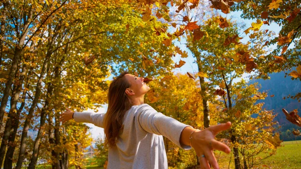 CLOSE UP: Cinematic shot of a carefree woman playing with dry tree leaves. — Stock Photo, Image