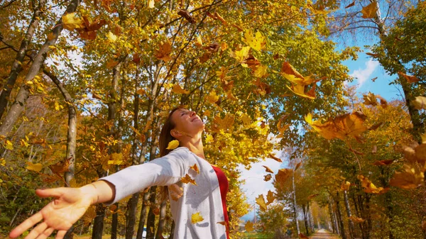 ZAMKNIJ SIĘ: Kobieta wyciąga ramiona jak złote liście spadają z daszków — Zdjęcie stockowe