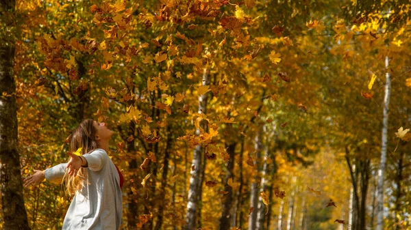 COPY SPACE: Smiling woman throws a heap of dry autumn colored leaves in the air.