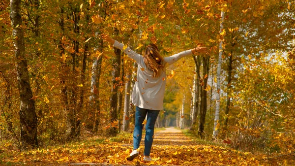 Nierozpoznawalna dziewczyna wyciąga ramiona po wyrzuceniu sterty suchych liści w powietrze — Zdjęcie stockowe