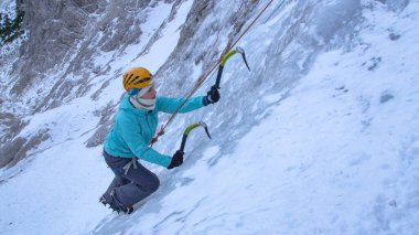 CLOSE UP: Young female alpinist scales up dangerous frozen waterfall in the Alps clipart