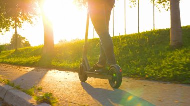 Gün batımında, kot pantolonlu bir kadının e-scooter sürerken ki görüntüsü..