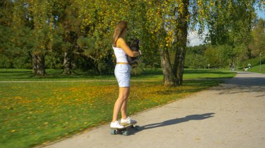Tanımlanamayan kadın kaykay sürerken köpeğini tutuyor.