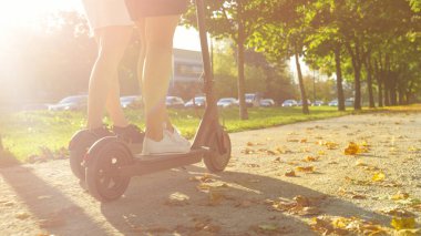 Tanımlanamayan iki bayan arkadaş, çakıllı yolda e-scooter kullanıyor..