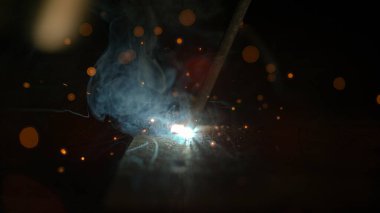 Atölyesinde çalışan kaynakçı karanlık metal yüzeyinde bir kaynak yapıyor..
