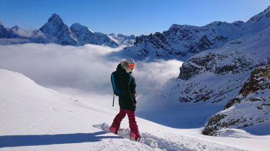 Neşeli dişi snowboardcu, inmeden önce karlı dağın tepesinde poz verir.