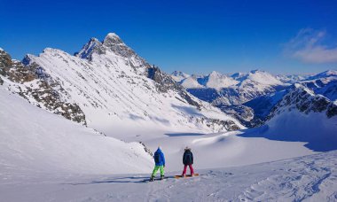 İki genç snowboardcu el değmemiş yamaçlara doğru hızla inmeden önce dağları gözlüyor.