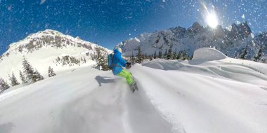 Kar taneleri güneş ışığında parlıyor, snowboardcu pistten çıkarken..