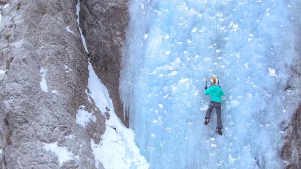 AERIAL: Mulher irreconhecível sobe uma bela cachoeira congelada nos Alpes. — Fotografia de Stock