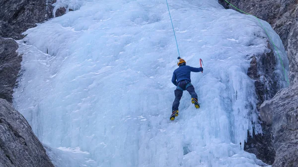 Αθλητικός άνθρωπος με κραμπόνια και άξονες πάγου κλιμακώνεται μέχρι το πανέμορφο παγωμένο καταρράκτη. — Φωτογραφία Αρχείου
