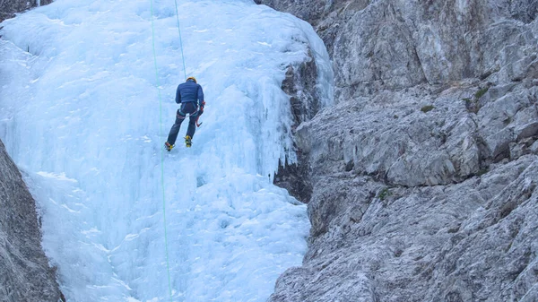 Montañero experimentado desciende por la cascada congelada después de escalarla. — Foto de Stock