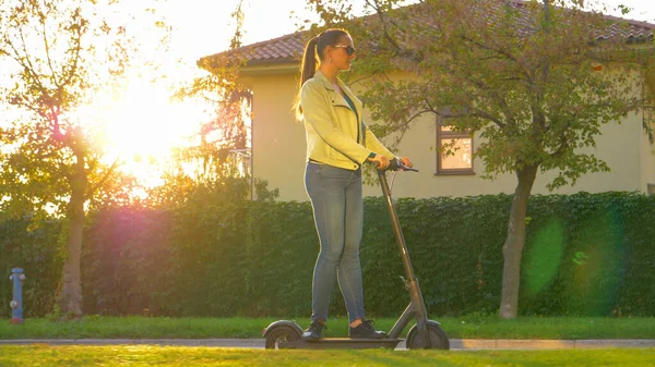 SOL FLARE: Millennial girl monta un e-scooter de alta tecnología por los suburbios. — Foto de Stock