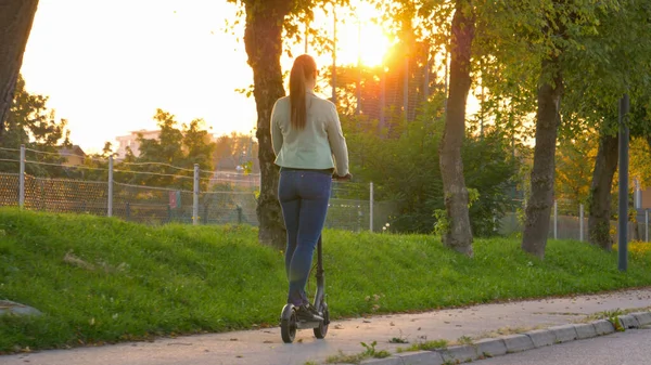 LENS FLARE Mujer monta un scooter eléctrico por una acera vacía en los suburbios — Foto de Stock