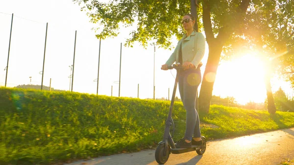 LOW ANGLE: Meisje dat plezier heeft op een elektrische scooter op een zonnige herfstavond. — Stockfoto