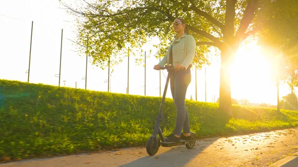 LOW ANGLE: Jonge vrouw rijdt een high-tech e-scooter langs een laan in de herfst. — Stockfoto