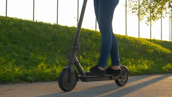 ÁNGULO BAJO: Mujer monta un scooter eléctrico por una acera vacía en los suburbios — Foto de Stock