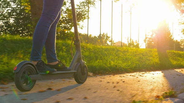 ΧΑΜΗΛΗ ΑΓΓΛΙΑ: Λεπτομερής θέα ενός e-scooter όπως σύγχρονες βόλτες κορίτσι μέσα από το πάρκο — Φωτογραφία Αρχείου