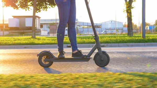 CLOSE UP Millennial in jeans speed down the empty road on a high tech e-scooter — Stok Foto