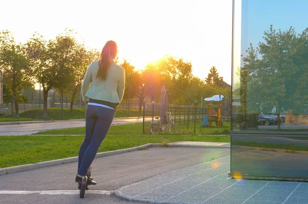 Güneş ışığı, camsı binanın etrafında scooter kullanan kadınlarda parıldıyor. — Stok fotoğraf