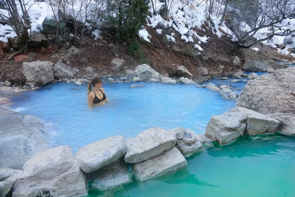 Jonge vrouw in bikini staat in een hete bron vijver en observeert de besneeuwde natuur. — Stockfoto