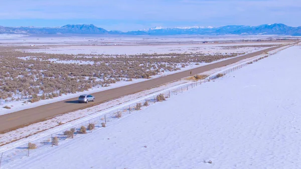 AERIAL: Zilveren SUV rijdt langs een schilderachtige interstate kruising besneeuwde Montana. — Stockfoto