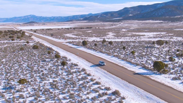 AERIAL: Rondrennen rond een auto als het rijdt over de besneeuwde vlaktes van Montana. — Stockfoto