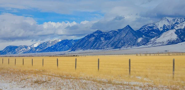 Cerca de arame farpado corre em torno de um pasto dourado sob as montanhas rochosas nevadas. — Fotografia de Stock