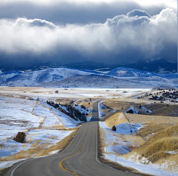 Nuvens tempestuosas escuras se reúnem acima da estrada rural que atravessa a pradaria de Montana — Fotografia de Stock