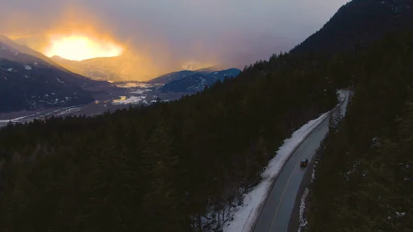 AERIAL: O céu da manhã de inverno se estende acima do carro dirigindo pela floresta no Canadá. — Fotografia de Stock