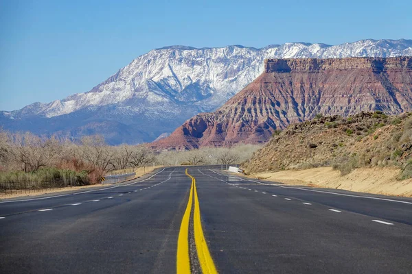 Низкий угол: Пустая дорога проходит через национальный парк и к заснеженным горам — стоковое фото