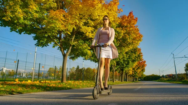 LOW ANGLE: Millennial rijdt e-scooter langs de weg langs de herfst gekleurde bomen. — Stockfoto
