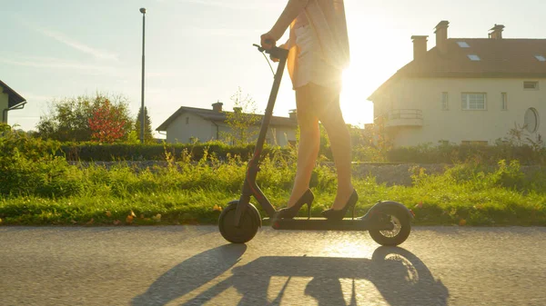 LOW ANGLE: Urban meisje in hakken rijdt elektrische scooter op een zonnige herfstochtend. — Stockfoto