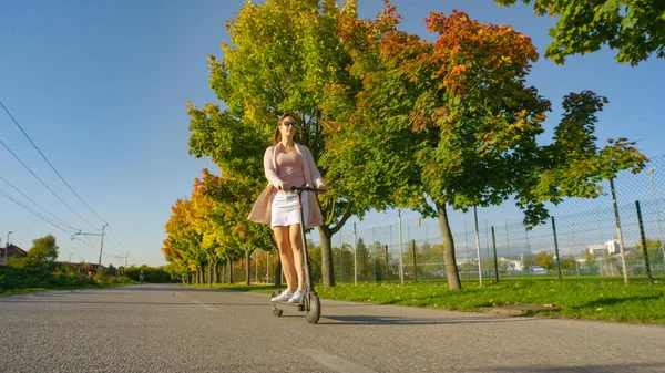 ÁNGULO BAJO: Mujer joven cruza a lo largo de la carretera de color otoño en la tarde soleada. — Foto de Stock