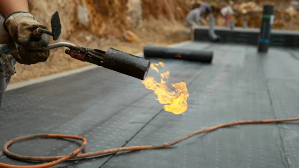 CLOSE UP: Строитель держит горящий факел после гидроизоляции здания. — стоковое фото