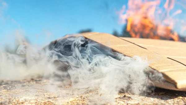 MACRO: Білий дим викидається зі складеного шматка картону, що горить на землі — стокове фото