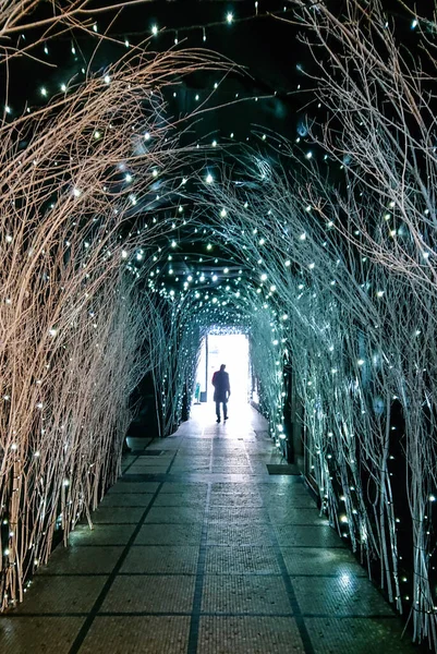 VERTICAL: Unrecognizable man walks out of a passageway full of Christmas lights. — Stockfoto